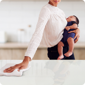 Mother wiping countertop while holding child in arm.